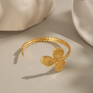 Détail macro d'un bracelet ouvert à fleur en acier plaqué or 18K sur support artistique blanc