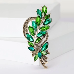 Detail of leaf brooch featuring green marquise crystals on a gold alloy base