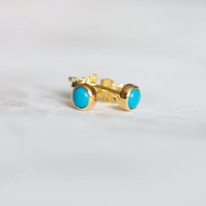Detailed view of gold flower earrings set with round turquoise stones on marble