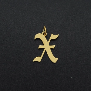 Macro shot of a gold-plated stainless steel letter X pendant charm on black textured surface
