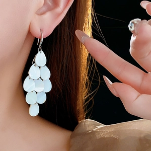 Detail of layered white teardrop shell pieces on long elegant drop earrings on model
