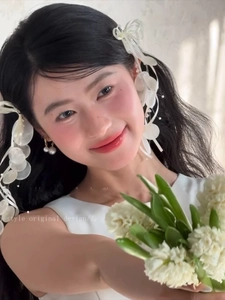 Detail of elegant white silk bow hair accessory and double pearl earrings on a model