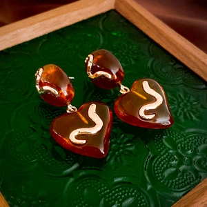 Macro view of heart-shaped resin earring with gold snake motif on green glass tray