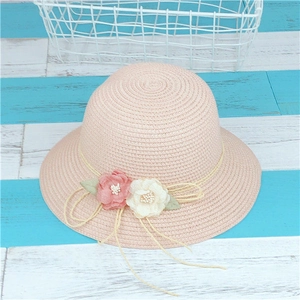 Détail d'un chapeau de paille rose avec fleurs décoratives en tissu et pompons tissés