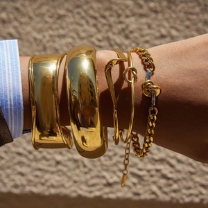 Gros plan de bracelets joncs et chaînes en acier inoxydable plaqué or 18k sur un poignet
