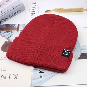 Close-up of a burgundy knit beanie with a woven logo tag on a minimalist magazine