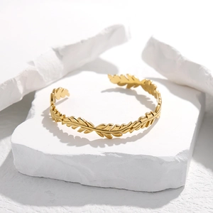 Dettaglio di un bracciale aperto dorato a forma di foglia su pietre decorative bianche
