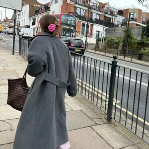 Street style view of a long dark grey wool coat with a pink flower hair claw clip accessory