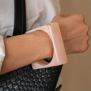Macro detail of a chunky pink marbled acrylic square bangle worn on a model wrist