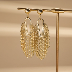 Close-up of golden tassel earrings with geometric triangle frames and fine bead chains
