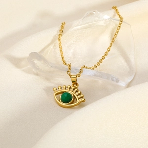 Minimalist gold evil eye pendant necklace with green stone on white silk background