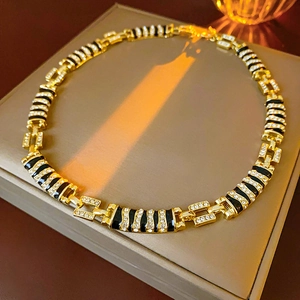 Detail of gold chain necklace with black enamel accents and diamond-encrusted charms