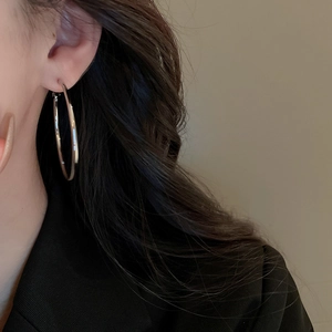 Side view detail of a large silver hoop earring worn by a model in a black blazer