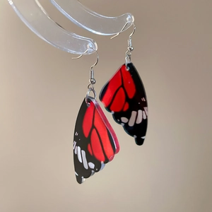 Detailed macro of acrylic monarch butterfly wing earrings on a semi-circular display