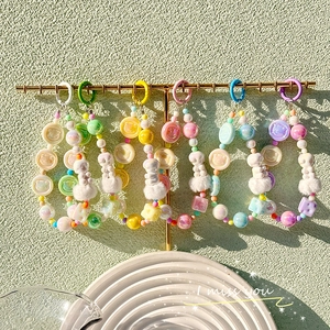 Colorful beaded bear keychain with pom-poms and bows hanging on a gold display stand