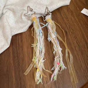 Gros plan de boucles d'oreilles étoile avec rubans à glands colorés sur bois et lin