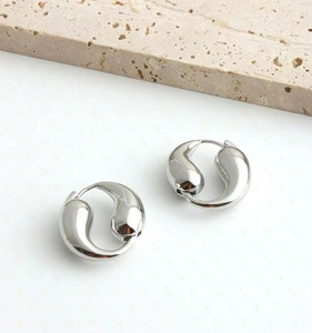 Macro detail of polished silver teardrop hoop earrings on minimalist stone background