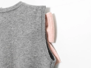 Dettaglio di un top grigio in maglia con fiocco rosa confetto lavorato a maglia sulla spalla