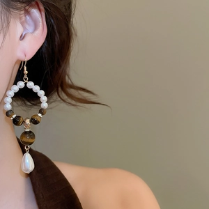 Close-up of vintage tiger eye and pearl drop earrings worn by a model in soft lighting