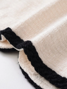 Vue détaillée de la texture du tissu en tweed crème avec bordure tressée noire décorative
