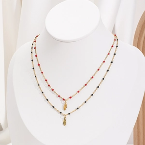 Close-up of double-layer gold necklace featuring red and black beads with leaf pendants