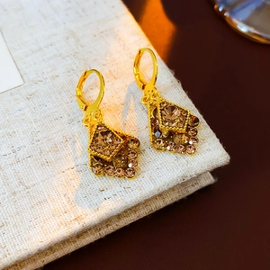 Macro shot of gold-finished earrings featuring amber rhinestones on beige fabric texture