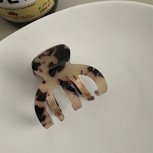 Detail of tortoiseshell acetate hair claw clip with golden metal inner teeth on ceramic tray