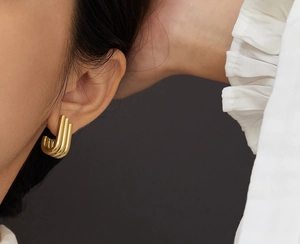Detailed close-up of triple-row gold hoop earrings worn on a model ear lobe