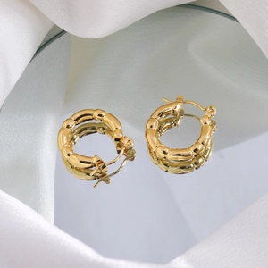 Close-up of golden bamboo texture hoop earrings on reflective mirror and white silk fabric