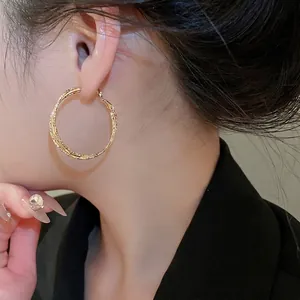Chic gold-layered geometric hoop earrings with textured finish worn by a model