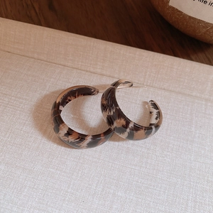 Macro shot of retro leopard print resin C-shaped hoop earrings on vintage fabric surface