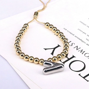 Detail of adjustable gold beaded bracelet with silver letter A charm and slider clasp