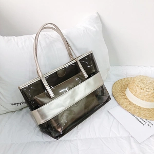 Smoky gray transparent PVC tote bag with champagne gold inner pouch on white bedding