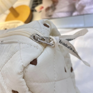 Detail of white quilted cosmetic bag with brown dots and ribbon zipper pull