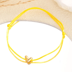 Bracelet tressé jaune ajustable avec breloque cœur doré sur une surface réfléchissante