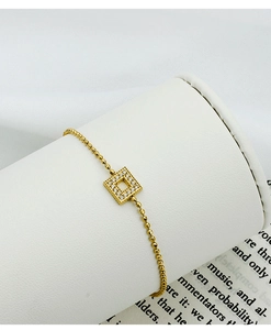 Close-up of golden ball chain bracelet with square zircon-encrusted pendant on a white stand