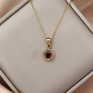 Detail of gold necklace with round red gemstone pendant surrounded by white zircon crystals