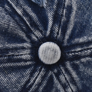 Macro shot of washed blue denim baseball cap top button and distressed frayed details