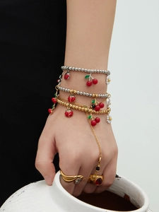Détail de bracelets en perles dorées avec breloques cerise et marguerite sur un poignet