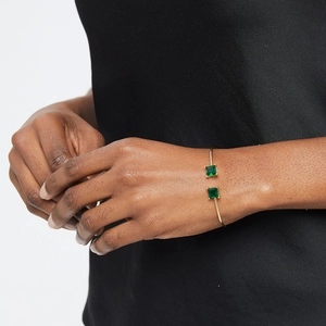 Elegant gold open cuff bracelet with two square green gemstones on female wrist