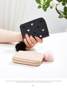 Close-up of small PU leather wallets with heart embroidery and fluffy pom pom zippers