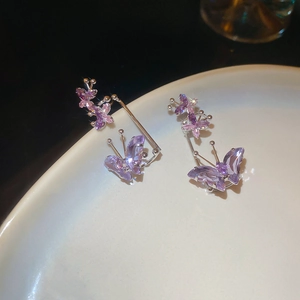 Macro detail of silver butterfly earrings with purple crystals on a white ceramic plate