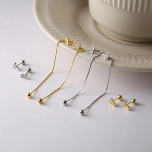 Elegant gold and silver heart stud earrings with sparkling zircons on ceramic tray