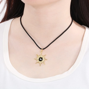 Gros plan détaillé du collier soleil doré avec gemme noire sur cordon noir