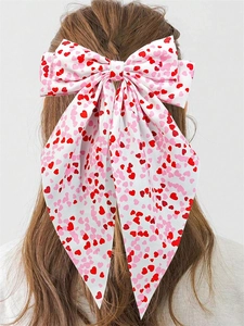 Detail view of large white bow hair clip featuring red and pink heart prints on fabric
