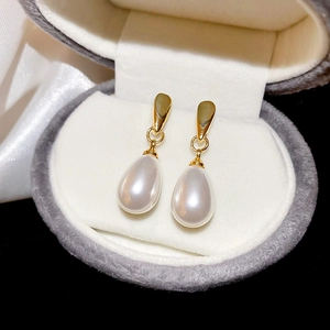 Detailed close-up of waterdrop pearl earrings with polished gold finish on grey velvet