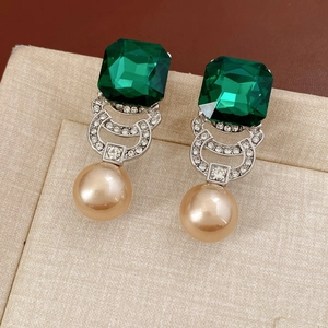 Dettaglio di orecchini vintage con gemma quadrata verde e goccia di perla champagne