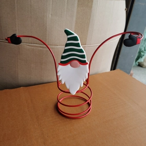 Detail of a Christmas gnome wine bottle holder with red metal arms and striped hat