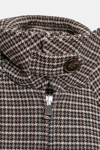 Detail of houndstooth jacket with stand collar, button strap and metal zipper
