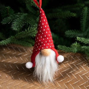 Red and white Christmas gnome ornament with knitted hat hanging on a green tree